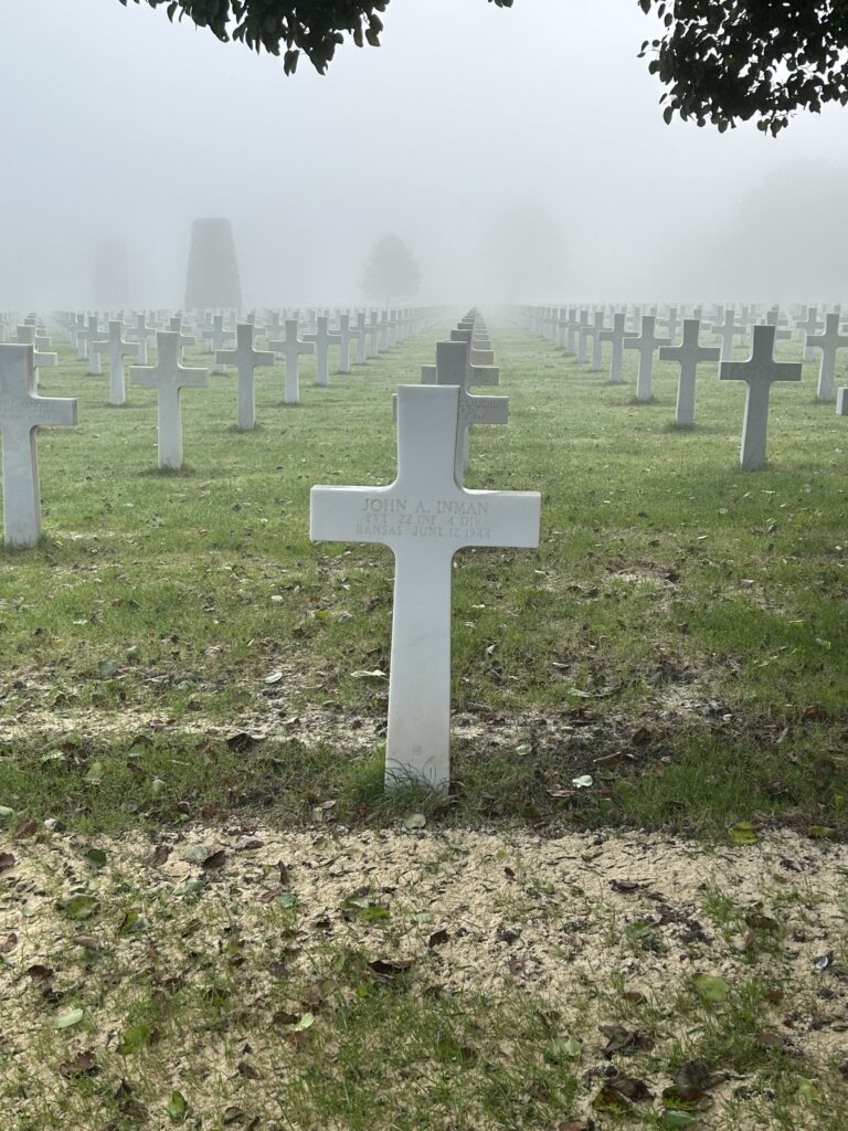 Many white crosses in the lawn of Normandy American Cemetery, with fog in the background.